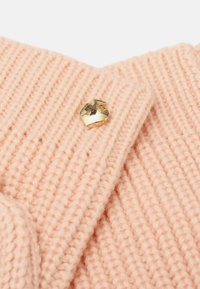 Primer plano de tejido de punto acanalado en rosa pálido con un pequeño pin en forma de corazón dorado y brillante adjunto.