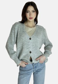 Grauer Strickcardigan mit V-Ausschnitt, verfügt über einen Knopfverschluss und gerippte Bündchen. Wird über einem hellen Oberteil getragen und mit blauen Jeans kombiniert.