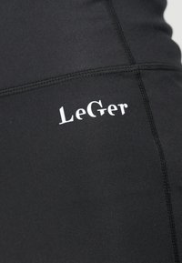 Pogled od blizu na crnu tkaninu s vidljivim šavovima i bijelim logotipom "LeGer" otisnutim na njoj.