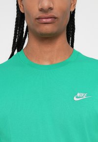 Πράσινο μπλουζάκι με στρογγυλή λαιμόκοψη, κατασκευασμένο από απαλό ύφασμα, με μικρό λευκό κεντητό λογότυπο της Nike στην αριστερή πλευρά του στήθους.