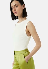 Biała prążkowana bluzka na ramiączkach bez rękawów, w połączeniu z gładkimi, zielonymi spodniami z wysokim stanem. Czyste linie i dopasowany krój.