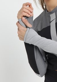Sportliches Langarmoberteil in Grau und Schwarz, mit gestreiften Ärmeln und tailliertem Design. Das Material hat eine glatte Oberfläche mit Elastan.