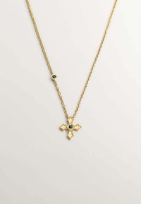 Collar de cadena de oro con un colgante de cruz decorativa que presenta un centro de piedra negra, superficie texturizada y pequeños acentos redondos.