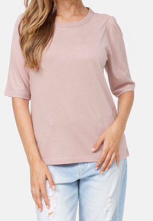 Bluzka z krótkim rękawem w jasnoróżowym kolorze, okrągły dekolt, miękka faktura i subtelne bufiaste rękawy, noszona z wystrzępionymi jasnoniebieskimi dżinsami.