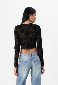 Fekete virágos csipkés, hosszú ujjú crop top, lekerekített nyakkivágással. Világoskék, magas derekú farmernadrággal párosítva, hátsó zsebekkel.
