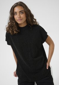 Top negru cu mânecă scurtă, cu guler înalt, dintr-un material texturat și cu o croială liberă. Prezintă modele subtile și o textură netedă.