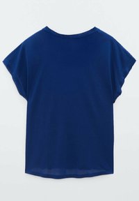 Chemise bleue à manches courtes, ample, avec un col rond, vue de dos sur un fond clair uni.