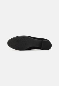 Chaussure plate noire avec un upper lisse et une semelle intérieure rembourrée. La semelle en caoutchouc présente un motif en spirale pour une meilleure adhérence et flexibilité.