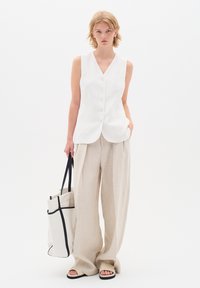 Vit ärmlös skjortblus som kombineras med beige vida byxor. Modellen bär en vit toteväska med svarta detaljer och har sandaler på fötterna.