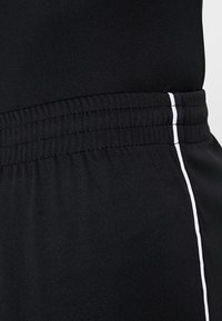 Mustat urheiluhousut, joissa on sileä pinta ja venyvä vyötärö. Valkoinen raita kulkee pystysuoraan sivussa tuomaan kontrastia.