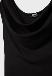 Schwarzes ärmelloses Oberteil mit drapiertem Ausschnitt, Nahaufnahme zeigt Stoffstruktur und Innenetikett mit der Aufschrift "strteen" Größe S, hergestellt in Bangladesch.