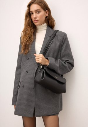 Sorte læder handbag med en buet top, sølvfarvet hardware og en skulderrem, parret med en grå stribet dobbeltknappet blazer.