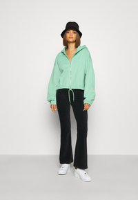 Mintgrøn cropped zip-up hoodie med snor, parret med sorte ribbede flared bukser og hvide sneakers. En sort bucket hat som tilbehør.