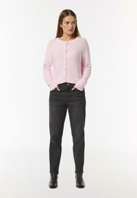 Light pink knitted cardigan with round neck, button closure, and ribbed cuffs, paired with dark high-waisted jeans and black ankle boots.