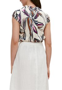Top de manga corta en crema con estampados llamativos en rosa, marrón y azul. Combinado con una falda blanca de cintura alta, con textura visible.