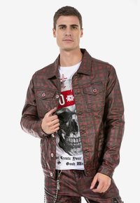 Rot-schwarz karierte Jacke mit metallischen Druckknöpfen, ausgestattet mit zwei Vordertaschen und einer glänzenden Textur, getragen über einem T-Shirt mit grafischem Totenschädel.
