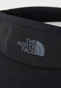 Črn klobuk z mrežastim vzorcem, izdelan iz lahko tkanine. Na sprednji strani prikazuje sivo logo "THE NORTH FACE".