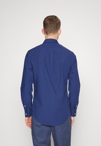 Camicia a maniche lunghe blu navy con colletto a bottoni, piega sul retro e orlo curvo, realizzata in un tessuto liscio di un colore uniforme.