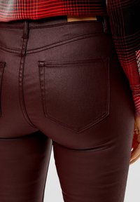 Vaqueros skinny burdeos con una textura suave, que cuentan con dos bolsillos traseros y un diseño ajustado; con un ligero brillo bajo la luz natural.