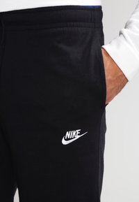 Svarta sweatpants i mjukt tyg, med elastisk midja och en vit Nike-logotyp på vänstra låret.