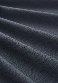 Tessuto grigio scuro con una superficie texturizzata caratterizzata da onde sottili e linee orizzontali, che mette in risalto il suo aspetto morbido e liscio.
