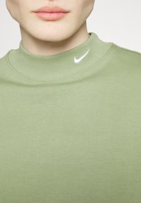 Gros plan d'une personne portant un haut vert clair à col montant avec un petit logo Nike swoosh blanc près du col.