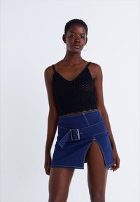 Top crop preto tricotado com bordas em forma de onda, combinado com uma saia mini de denim azul com uma fenda frontal e um cinto largo com uma fivela prateada.