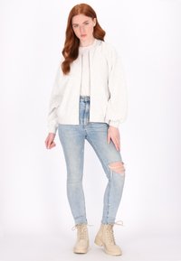 Světlé šedé bomber jacket s předním zipem, žebrovanými manžetami a volným střihem, kombinované se světlými modrými potrhanými skinny džíny a béžovými šněrovacími botami.
