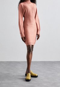 Robe pull tricotée, à manches longues, col roulé en rose poussiéreux, design ajusté, coutures latérales, associée à des sabots jaunes à enfiler avec des semelles noires.