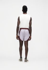 Shorts bordeaux à motif géométrique blanc, taille élastique et poches latérales, assortis à un débardeur blanc.