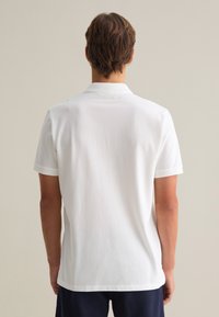 Camisa polo blanca de manga corta con un cuello clásico, fabricada en algodón suave y con un corte relajado. Presenta una parte posterior limpia sin adornos.