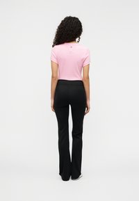 Ρο ζ τοπ με κοντά μανίκια και λογότυπο στο πίσω μέρος, σε συνδυασμό με μαύρο παντελόνι καμπάνα. Λεπτό ύφασμα με εφαρμοστή γραμμή.