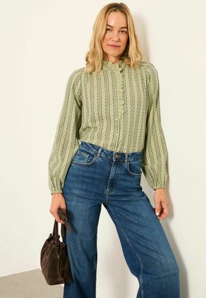 Green patterned blouse with ruffled collar and button closure, paired with high-waisted blue jeans and a small dark brown bag.