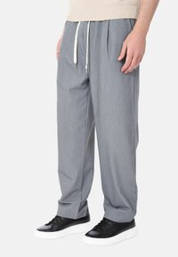 Pantaloni grigi a vestibilità comoda con vita regolabile, pieghe frontali e una texture leggera, abbinati a sneakers in bianco e nero.