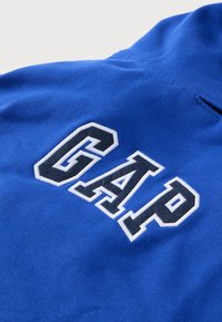 Niebieska bluza z haftowanym logo „GAP” w kolorach białym i ciemnoniebieskim. Miękki materiał, okrągły dekolt i gładka faktura.