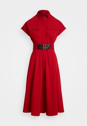 Punane puuvillane kleit, millel on krae, lühikesed varrukad, kaks rinnataskut ja must vöökoht. Laienev seelik ulatub keskmise sääre pikkuseni.