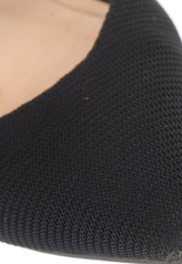 Gros plan d'un tissu noir texturé avec une petite tache brune à la surface.