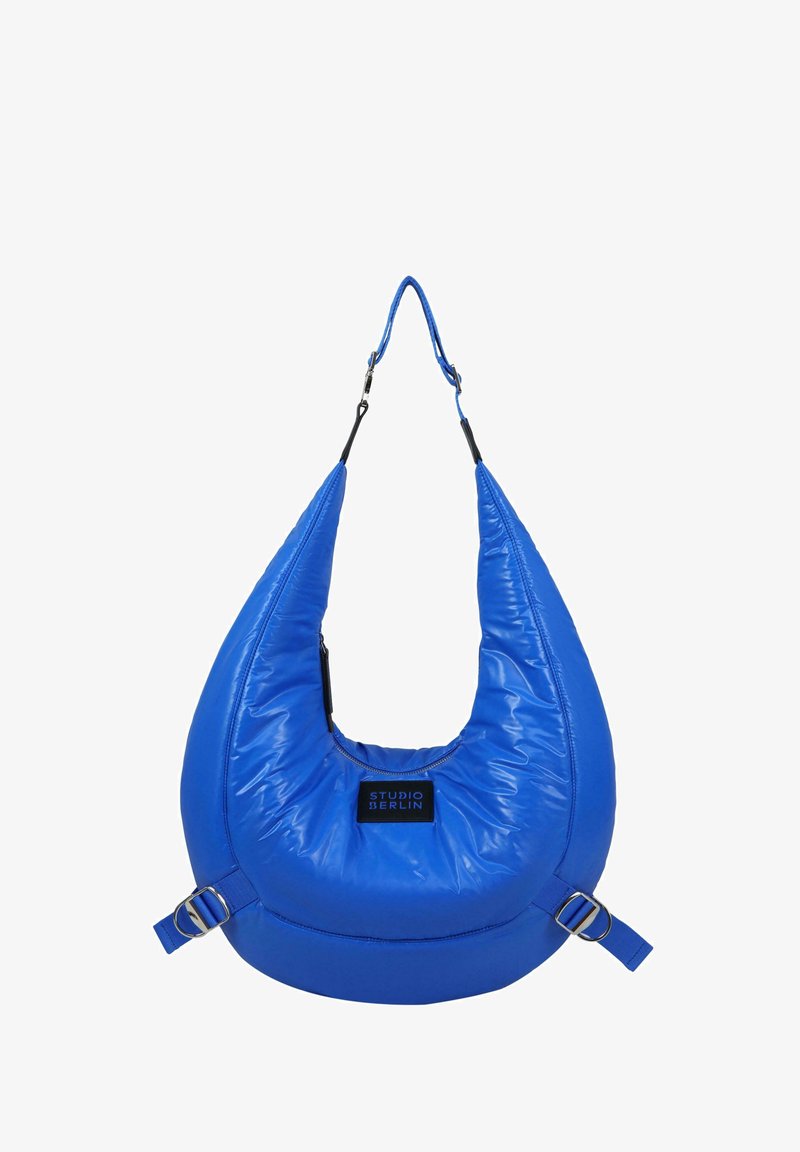 Bolso hobo azul acolchado con un acabado brillante, que cuenta con una correa ancha, un cierre de cremallera y una etiqueta rectangular en el frente.