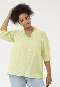 Blusa amarilla claro con escote con volantes y mangas tres cuartos. Presenta un patrón texturizado en zigzag en toda la prenda.