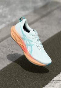 Lyseblå løpesko med mesh-overdel, oransje mellomsåle, turkise detaljer og et teksturert mønster på siden, designet for komfort og støtte.