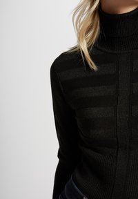 Pull col roulé noir avec un motif côtelé texturé et une légère brillance, offrant une coupe ajustée et des manches longues.
