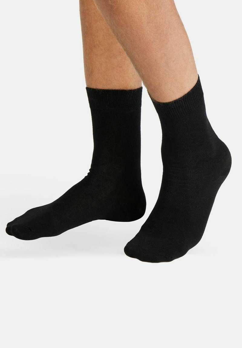Black ankle socks with a smooth texture, ribbed cuff, and seamless design, showcasing a fitted shape that conforms to the foot.