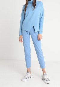 Vaaleansininen asu, jossa on epäsymmetrinen pitkähihainen paita ja kapeat housut, yhdistettynä valkoisiin lenkkareihin. Sileä rakenne, rento tyyli.