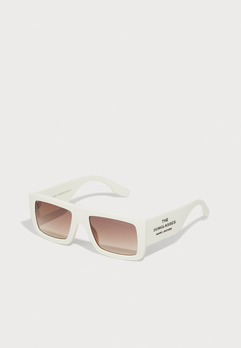 Biele obdĺžnikové slnečné okuliare s hnedým gradientným sklom, plochý rám a text „THE SUNGLASSES MARC JACOBS“ na nožičkách.