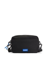 Bolso bandolera negro de nailon con una textura lisa, forma rectangular, cierre de cremallera y un destacado logo azul de "HUGO" en la parte frontal.