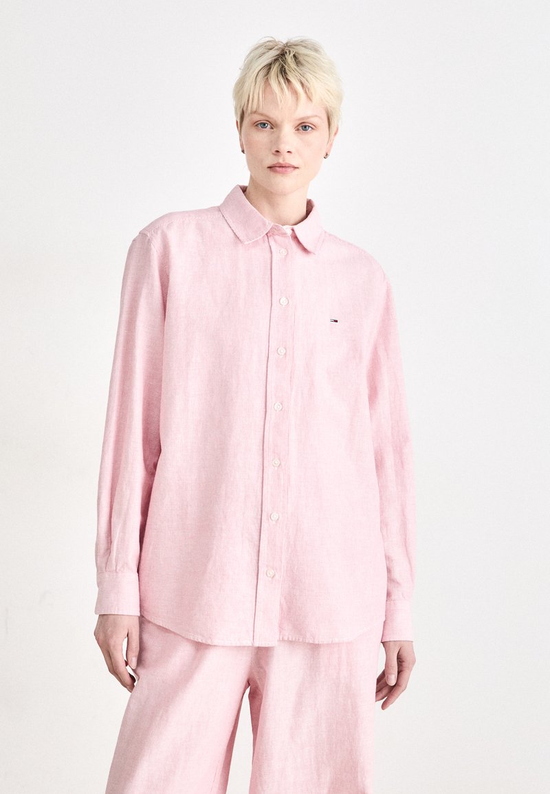 Light pink long-sleeve button-up shirt with a pointed collar and subtle texture. Small logo detail on the left chest, paired with matching pants.
