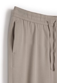 Jasnobeżowe spodnie sportowe wykonane z miękkiego materiału, z elastycznym pasem ze sznurkiem i bocznymi kieszeniami. Gładka faktura.