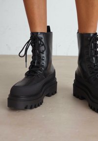 Bottines noires à lacets en cuir lisse avec une semelle plateforme épaisse et striée, comportant des �œillets et des panneaux texturés.