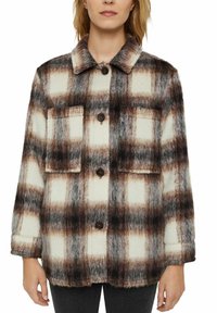 Rutigt shacket i mjukt, texturerat tyg; har ett rutmönster i brunt, vitt och grått, två bröstfickor och framknäppning.