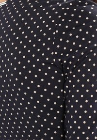 Tissu bleu marine avec un motif à pois blancs. Présente une texture lisse et un col rond classique.